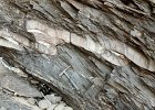 c97-10  Asymmetric folds in a sandy layer with brittle rupture and quartz vein fillings. Slaty cleavage in the intervening fine-grained rock is approximately axial-planar to the folds. Cornwall.